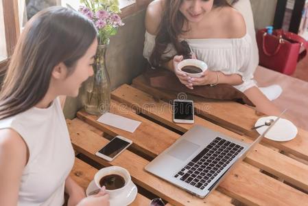 两个十几岁的女人相遇采用咖啡豆商店使用智能手机和便携式电脑