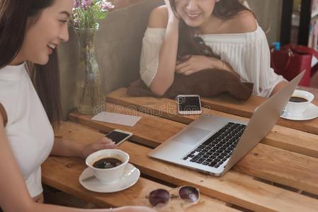 两个十几岁的女人相遇采用咖啡豆商店使用智能手机和便携式电脑