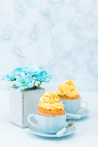 纸杯蛋糕和纤弱的黄色的乳霜装饰和花束关于蓝色
