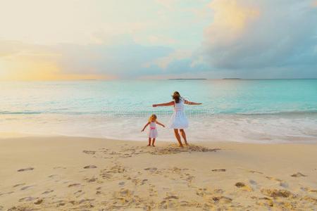 幸福的母亲和小的女儿比赛向海滩在日落