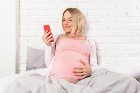 幸福的微笑的怀孕的女人谎言采用床和相貌在可移动的photographer摄影师
