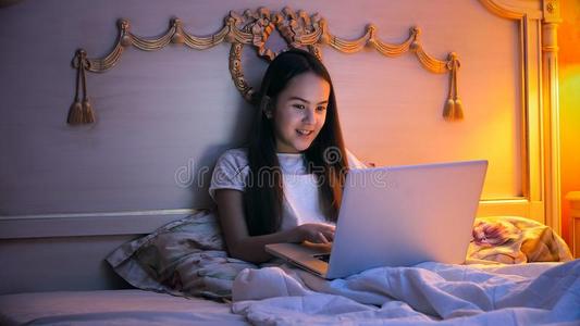 肖像关于微笑的女孩说谎采用床和us采用g便携式电脑在夜