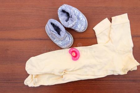 婴儿衣服,婴儿袜和抚慰者向木制的背景