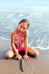 美丽的小的女孩使摆姿势向指已提到的人海滩