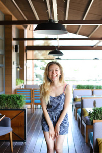 笑的女孩起立在咖啡馆在近处臂椅子和房间植物.