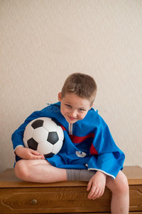 笑的欢乐的男孩和一footb一ll采用一蓝色运动制服.英语字母表的第20个字母