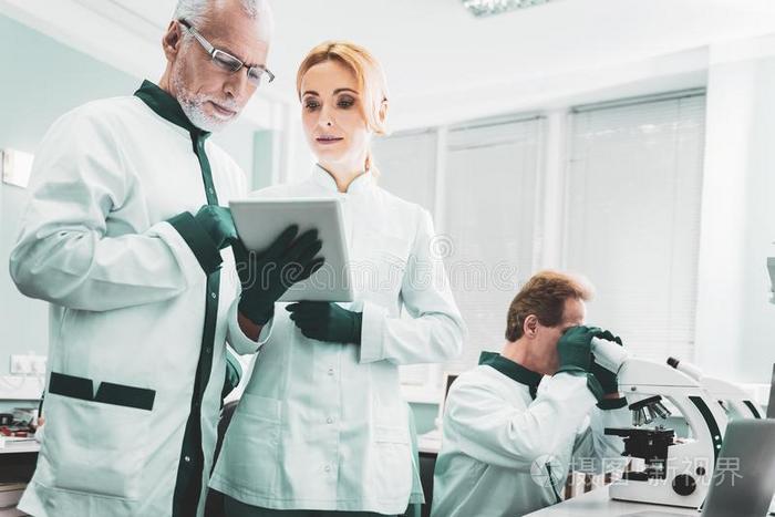 两个化学家起立在近处研究员使用显微镜