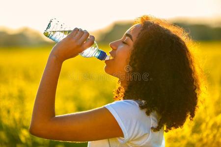 混合的赛跑非洲的美国人女孩十几岁的青少年喝饮料水在日照片