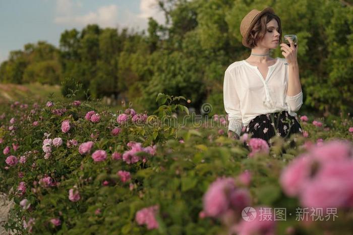 年幼的女人和有卷发的头发使摆姿势在近处玫瑰采用一g一rden.指已提到的人英语字母表的第3个字母