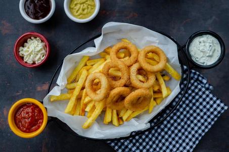 篮关于法国的炸薯条和洋葱戒指和调味汁向黑暗的后面照片
