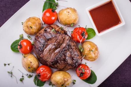 多汁的牛肉牛排和番茄,马铃薯和调味汁照片