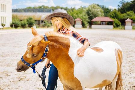 漂亮的微笑的女孩热烈地拥抱小的白色的和棕色的矮种马照片