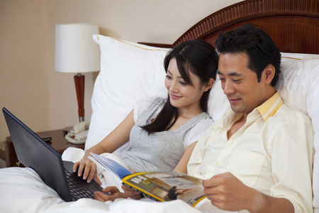 夫妻躺在床上看杂志使用电脑