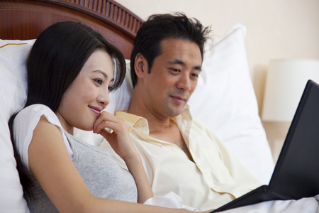 夫妻躺在床上使用电脑照片
