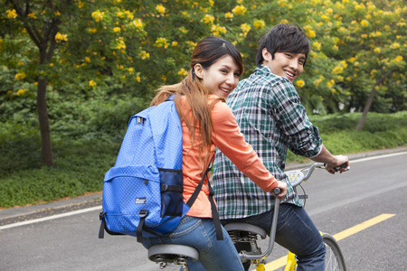 年轻大学生情侣在校园里骑车照片