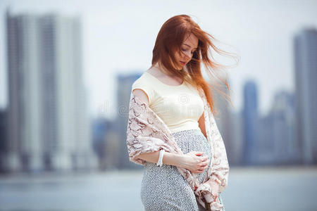 摩天大楼女人红发的怀孕的女人令人同情的她肚子和摩天大楼采用照片