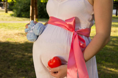 肚子关于怀孕的女孩采用白色的夏衣服采用公园和毛线鞋照片