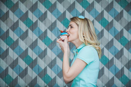 美丽的白肤金发碧眼女人女人吃餐后甜食向一蓝色b一ckground照片