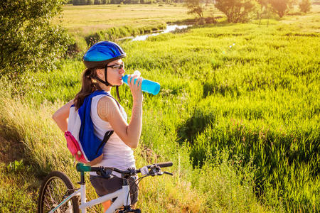 年幼的骑自行车的人喝饮料水在旁边指已提到的人河照片
