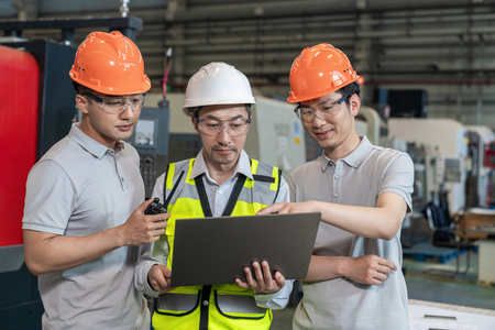 三个工程师穿保护工作服戴着安全帽在工厂工作照片