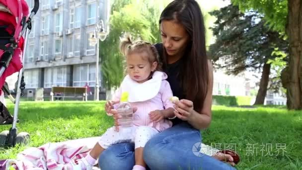 年轻漂亮的妈妈喂孩子在 park.young 母亲与婴儿午餐上 grass.mom 饲料在公园里拍孩子在我母亲旁边的公园里的小女