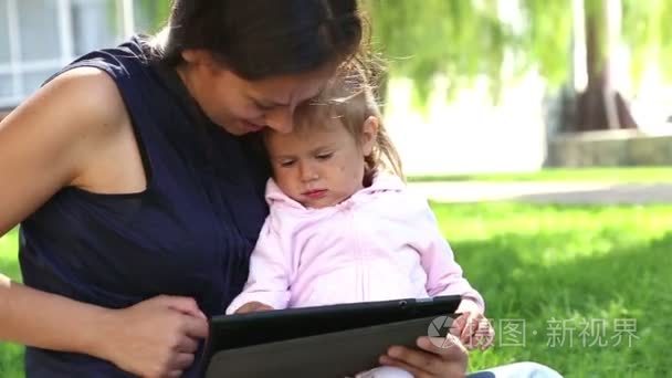 妈妈教小 girl.mom 教孩子玩孩子在公园里玩便携式计算机上的 tablet.young 妈妈