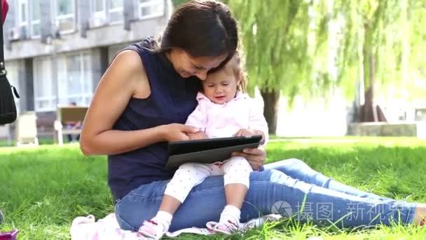 妈妈教小 girl.mom 教孩子玩孩子在公园里玩便携式计算机上的 tablet.young 妈妈