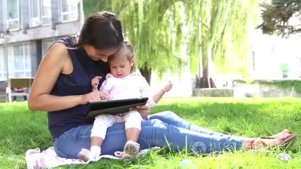 妈妈教小 girl.mom 教孩子玩孩子在公园里玩便携式计算机上的 tablet.young 妈妈