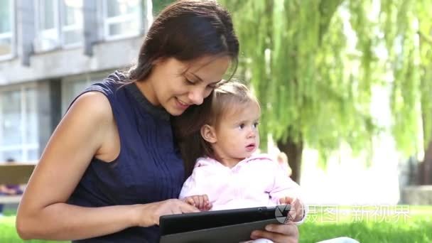 妈妈教小 girl.mom 教孩子玩孩子在公园里玩便携式计算机上的 tablet.young 妈妈