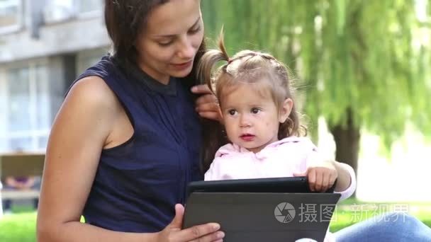 妈妈教小 girl.mom 教孩子玩孩子在公园里玩便携式计算机上的 tablet.young 妈妈