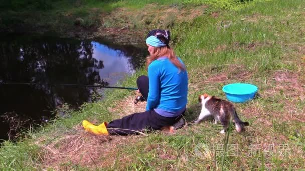 怀孕的女孩坐在湖岸上和捕鱼的可爱猫咪