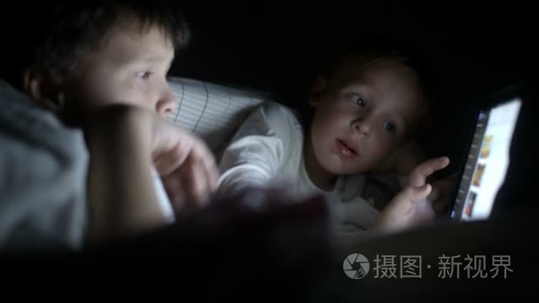 两个小男孩试着在晚上使用这款平板电脑看电影视频