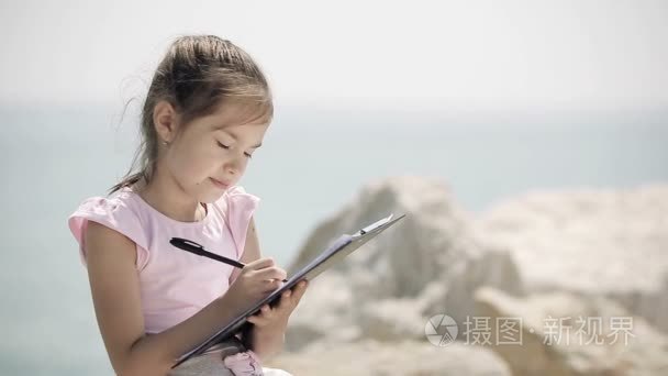 一个孩子坐在一块石头上靠近亚得里亚海和画一幅画视频
