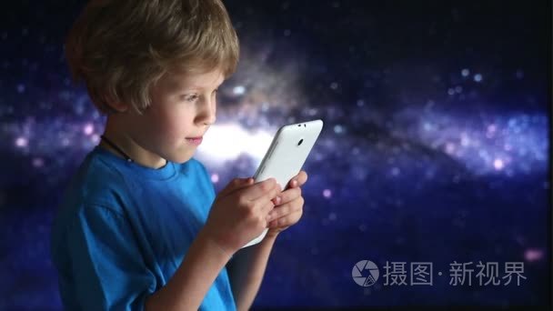 男孩玩平板电脑。男孩和平板设备中坐在宇宙星空背景上的手的特写