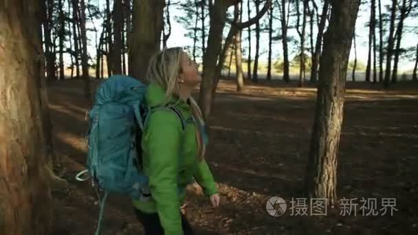 徒步旅行者金发女郎走在森林与背包徒步旅行。开枪的替身