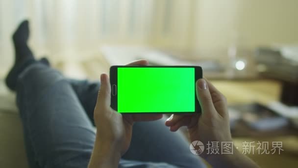 男人放在家里的沙发上，抱着 Android 手机与绿色屏幕在横向模式