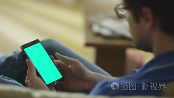 男人放在家里的沙发上和与绿色屏幕在肖像模式下使用 Android 手机