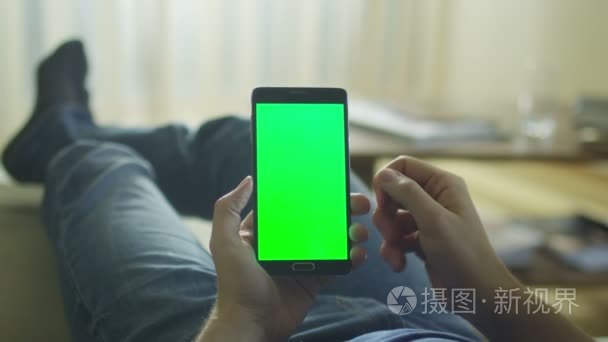 Man is Laying on Couch at Home and Using Android Phone with Gree