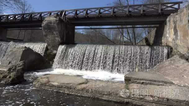 ripply waterfall with wooden bridge in park.