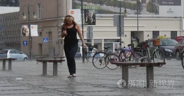 金发女人，黑色的衬衫和黑裤子跑在雨汽车建设和自行车停车场的背景多云的天气倾盆大雨景观