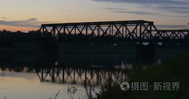 河池塘荡漾水桥河的树的剪影反射明亮的日落粉红色和黄色的天空树在地平线上