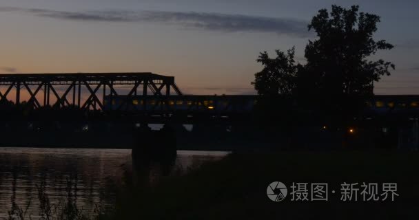 火车是移动桥河池塘桥通过河荡漾水中树木的轮廓反射光明日落粉红色和黄色的天空