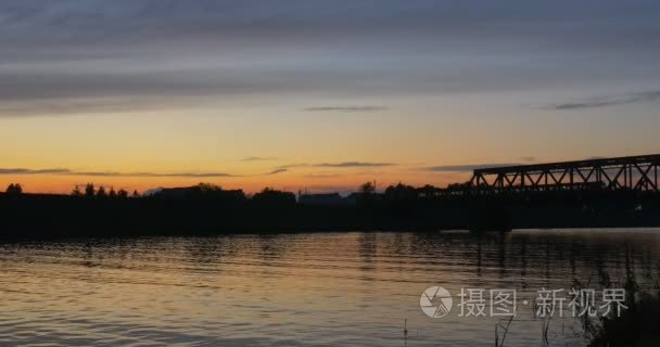 火车是移动的桥河人骑着自行车在地平线荡漾水树木剪影反射光明日落粉红色和黄色的天空