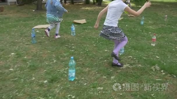 Two Girls Play Run Around The Bottles On The Grass