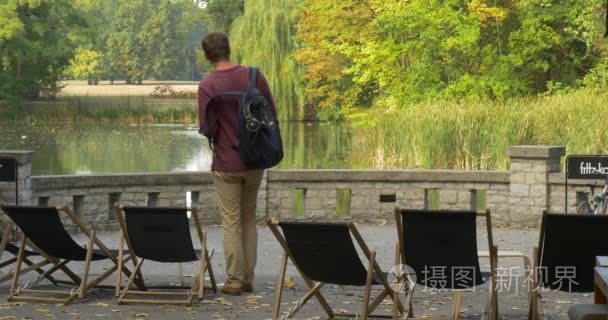 人来到躺椅上他脱下他的背包里，把它放在地上的男人坐在椅子和望湖公园区湖绿色树木