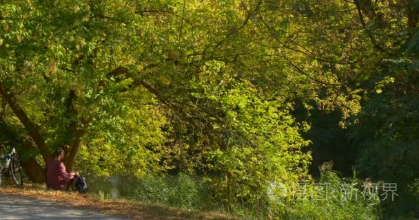 Man Sits Down On The Ground Under Spreading Green Tree And Puts 