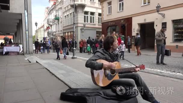 adult man play with mouthorgan and guitar and people walk. 4K