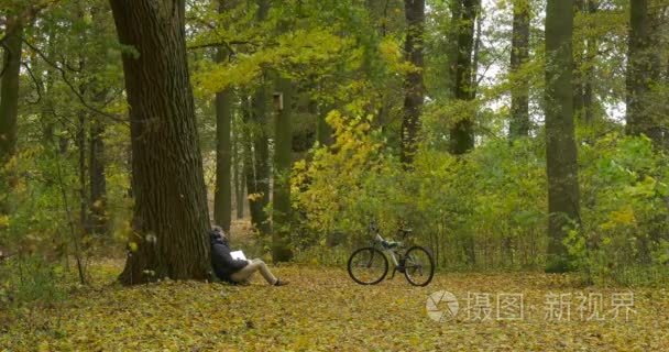 在温暖 Ushanka 帽子的男人与笔记本电脑自由职业者程序员文案设计师会计人正坐在树工作下降叶秋