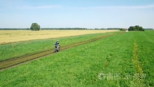 空中  年轻人骑自行车在农村公路通过绿色和黄色字段