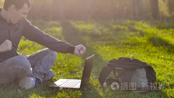 坐在绿草的生活方式草坪阳光对笔记本人学生惊喜欢乐